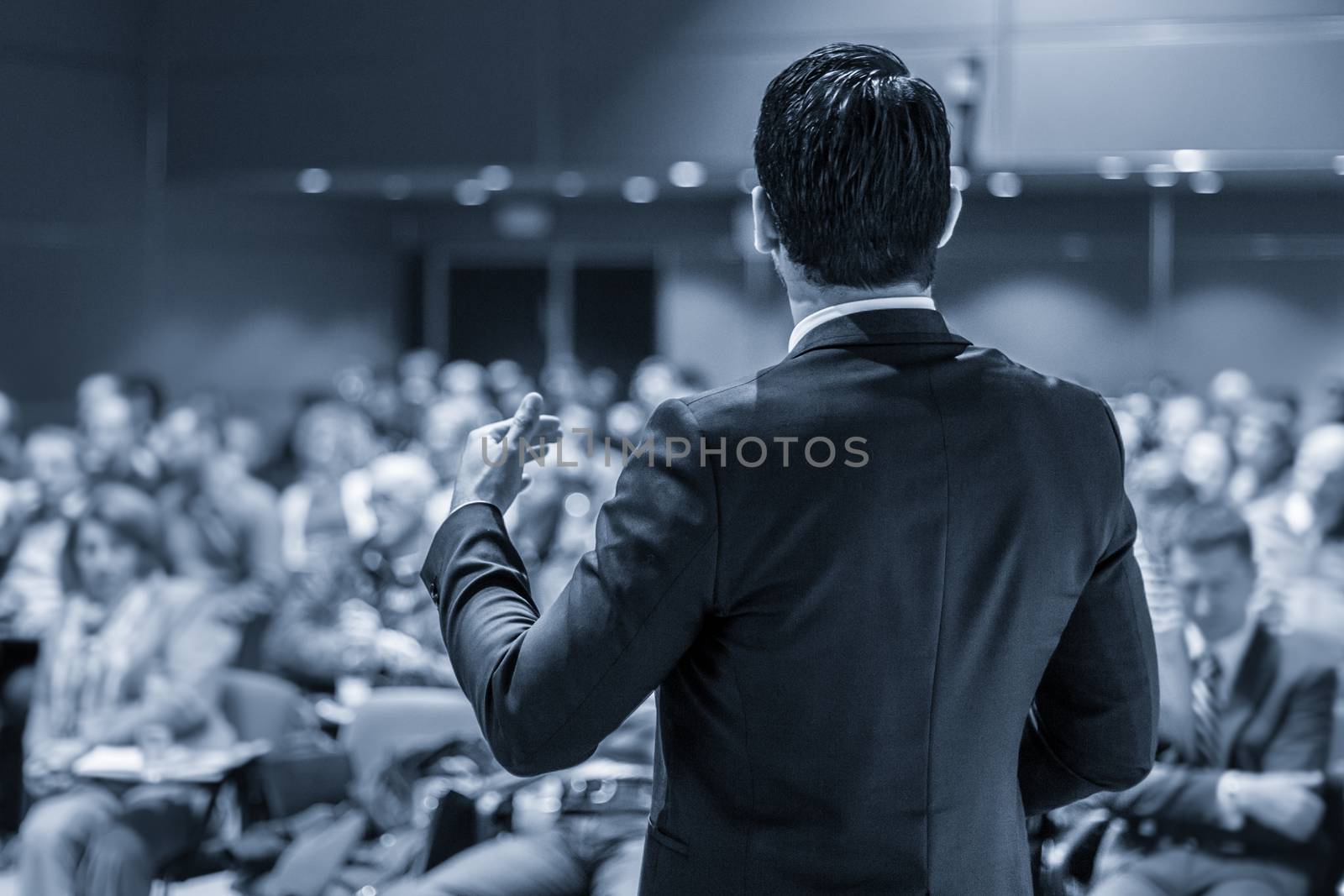 Speaker at Business Conference with Public Presentations. Audience at the conference hall. Entrepreneurship club. Rear view. Panoramic composition. Blue toned greyscale.