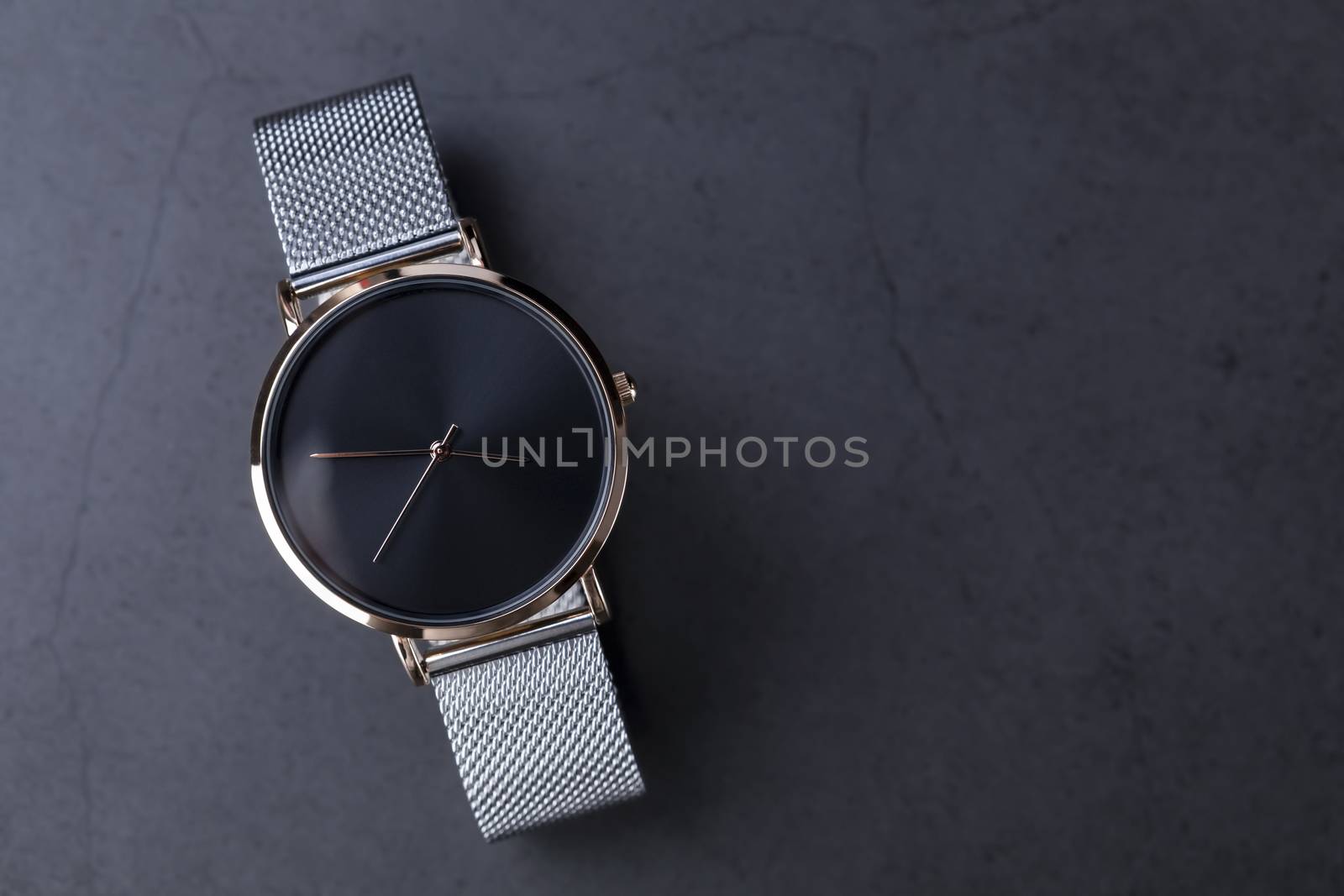 Black wrist watch for women with metal bracelet on black background.