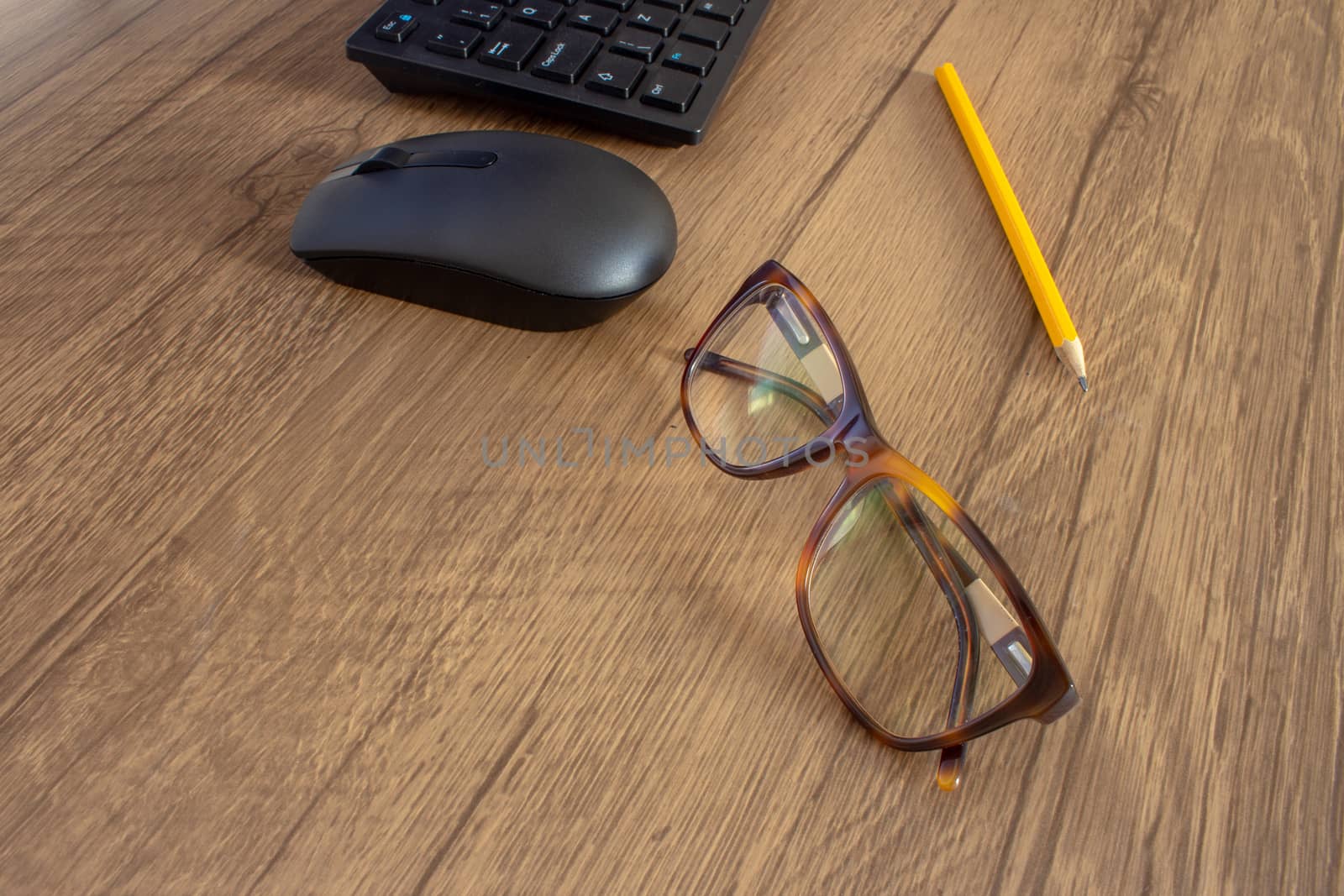 Par of glasses next to a pencil, a mouse and keyboard on top of a wooden desk