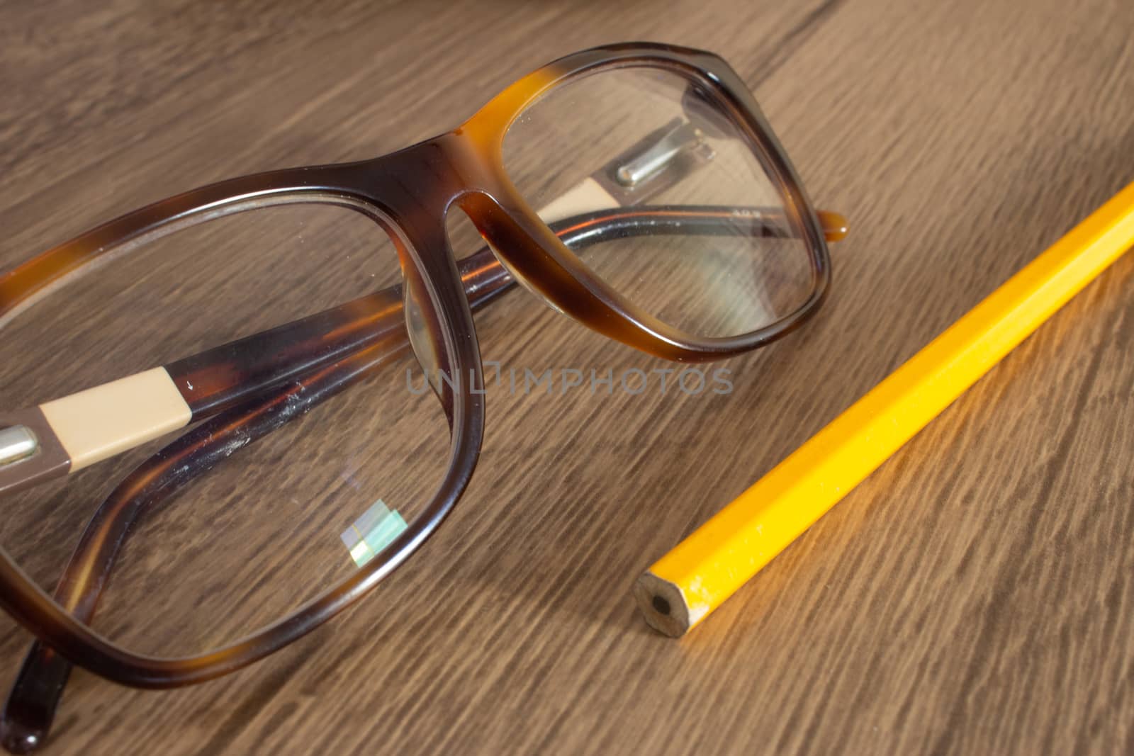 Par of glasses and a pencil on top of a wooden table