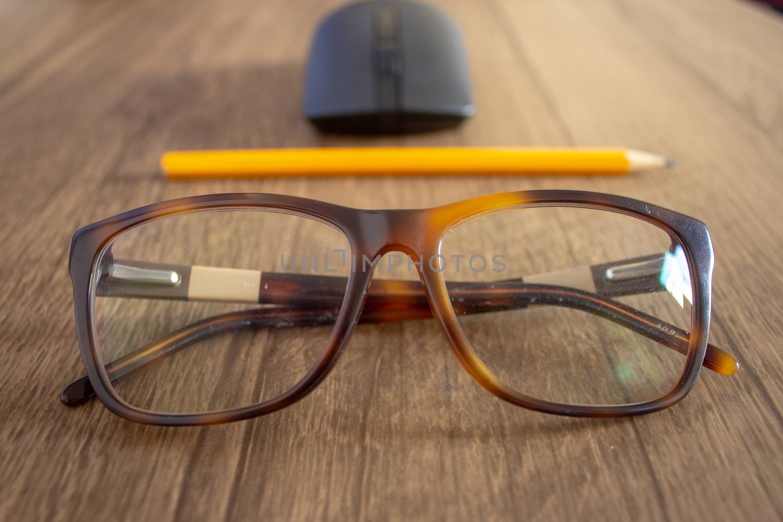 Closeup on a par of glasses with a pencil and mouse on the background, on top of a wooden table