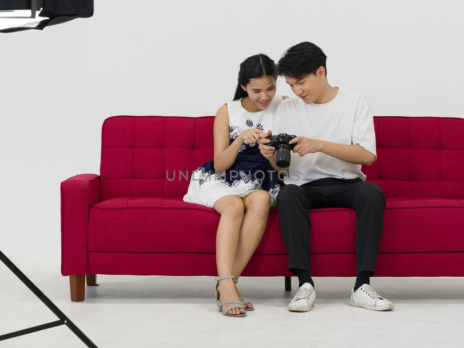 Asian photographers allow models to view pictures taken on the camera screen while sitting on a red sofa. Working atmosphere in the photo studio