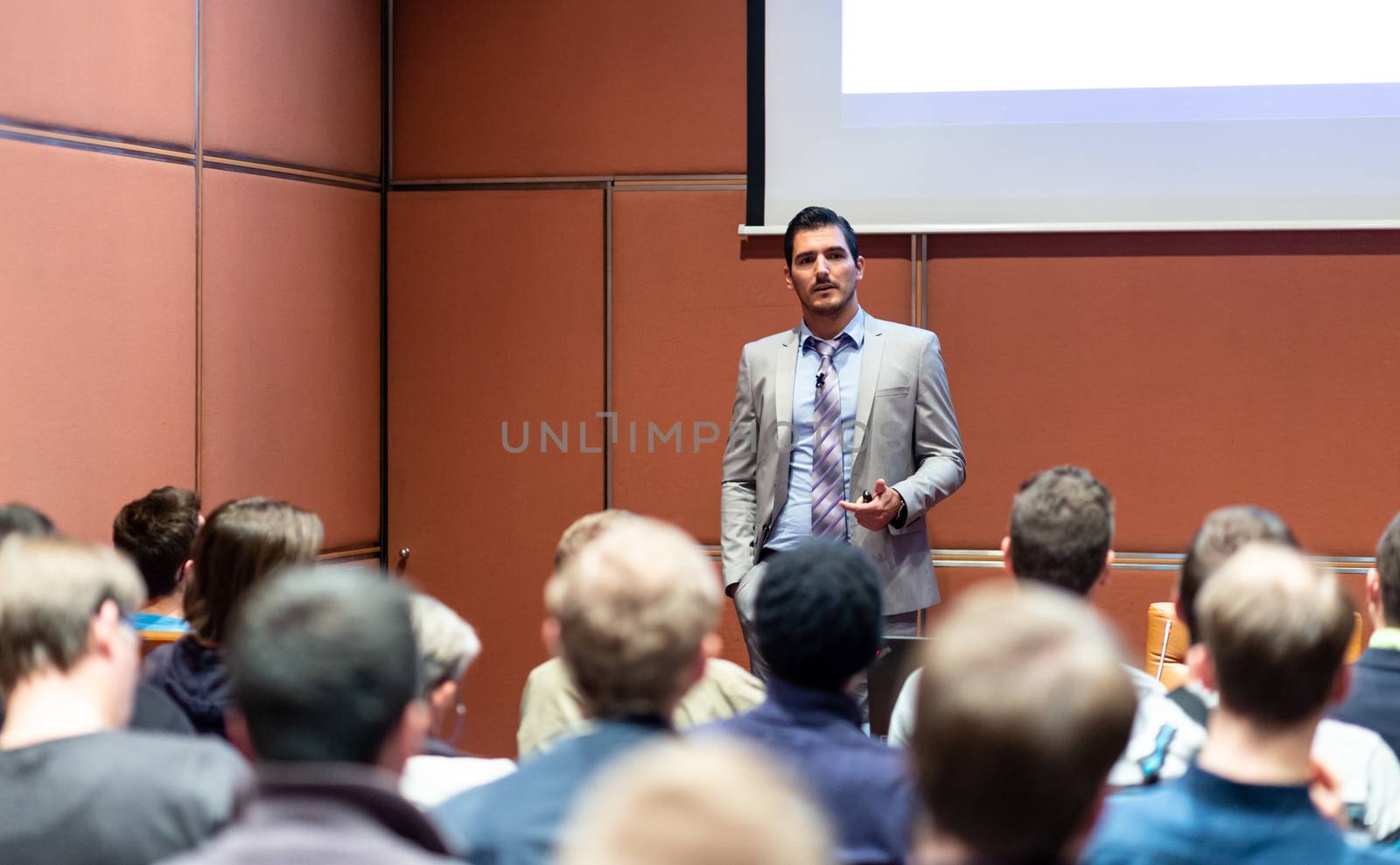 Speaker giving a talk in conference hall at business meeting event. Rear view of unrecognizable people in audience at the conference hall. Business and entrepreneurship concept.