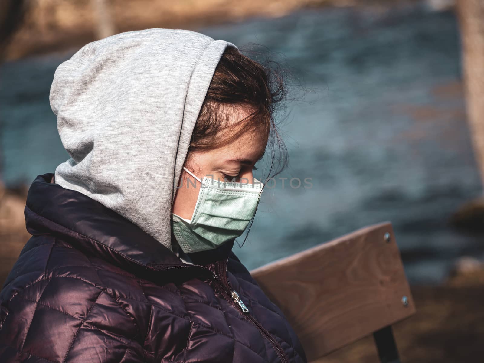 Lady and coronavirus protection. Sad Woman sitting alone on bench in park wearing mask to avoid infectious. Corona virus, or Covid 19, is spreading all over the world. Receives bad news on her phone.