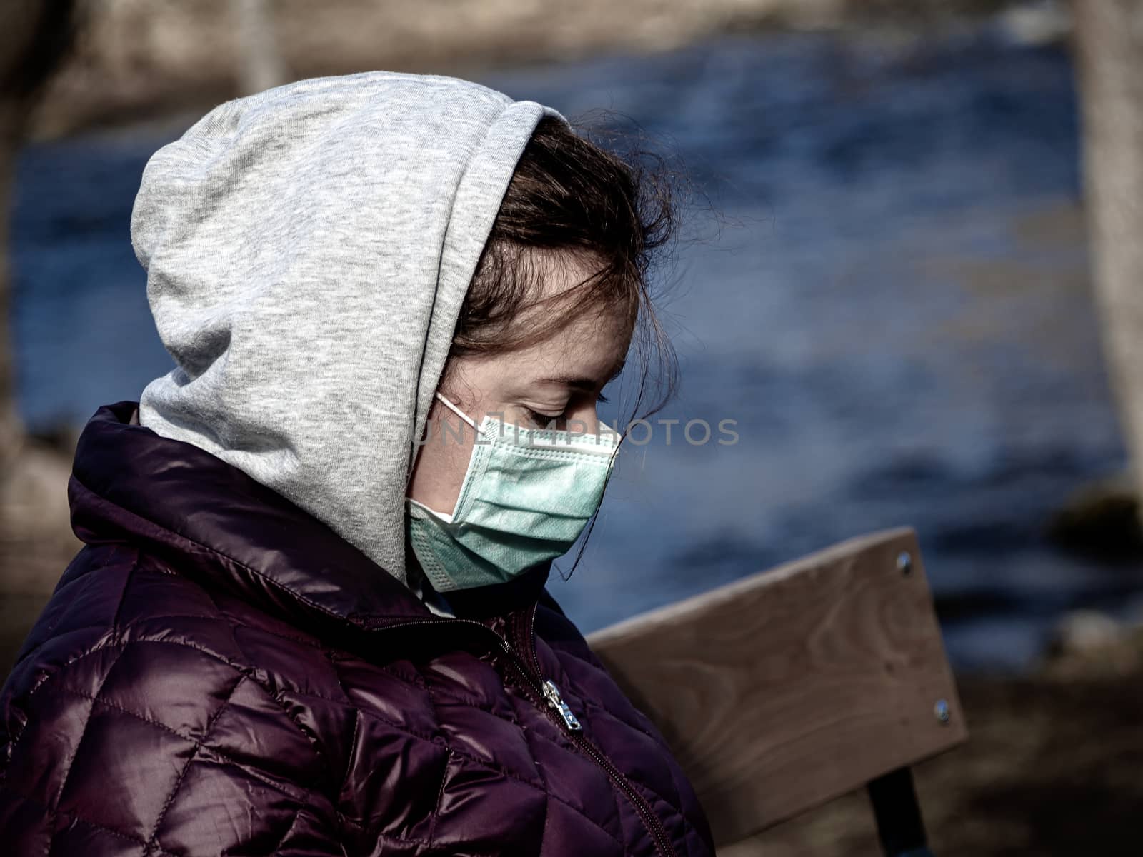 Lady and coronavirus protection. Sad Woman sitting alone on bench in park wearing mask to avoid infectious. Corona virus, or Covid 19, is spreading all over the world. Receives bad news on her phone.