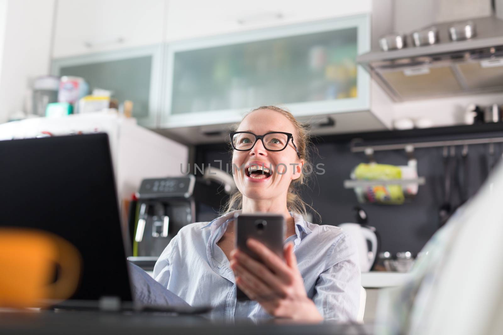 Stay at home and social distancing. Woman in her casual home clothing working remotly from kitchen dining table. Video chatting using social media with friend, family, business clients or partners.