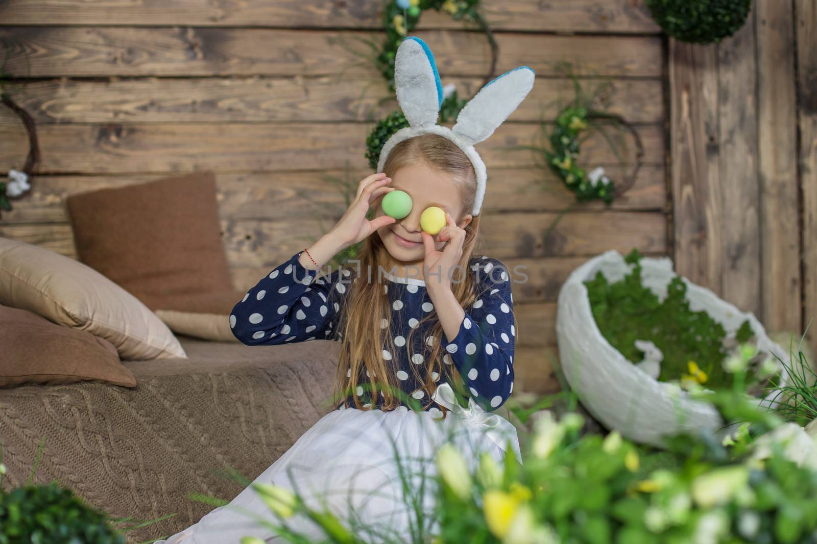 
Funny portrait of girl having fun on Easter wearing bunny ears and holding eggs on eyes during spring season
