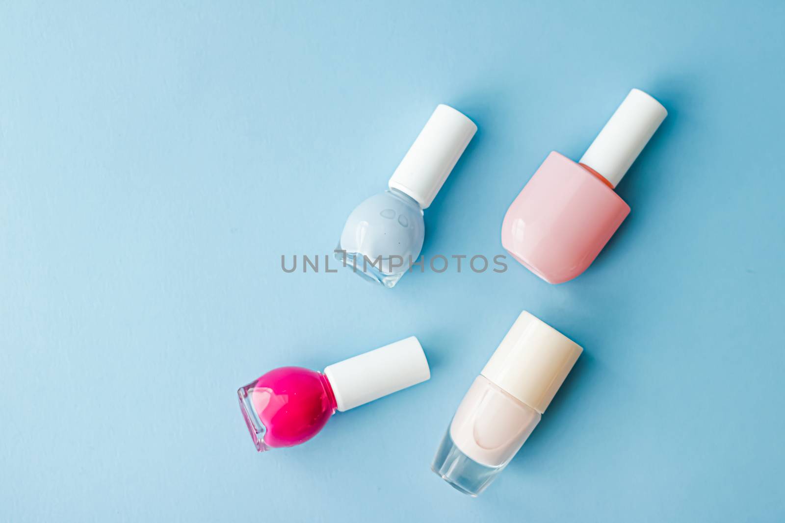 Colourful nail polish bottles on blue background, organic make-u by Anneleven