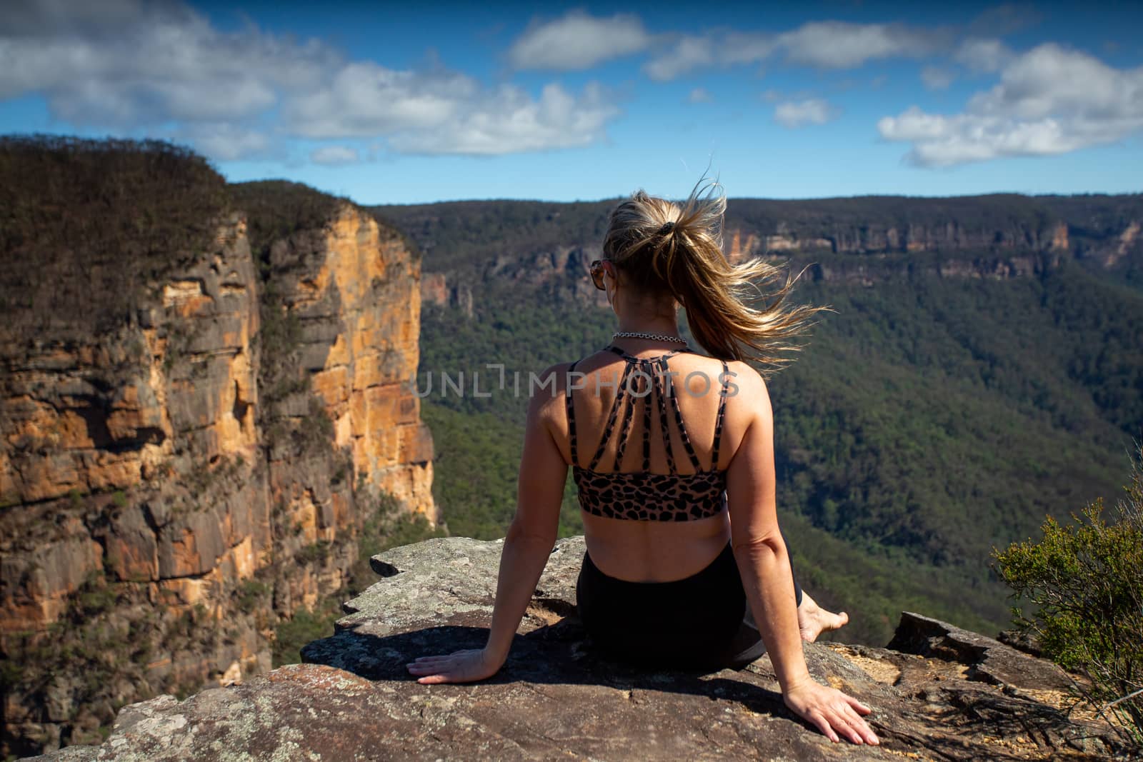 Woman relaxing on a cliff with scenic mountain and valley views.  Her pony tail blowing in the wind