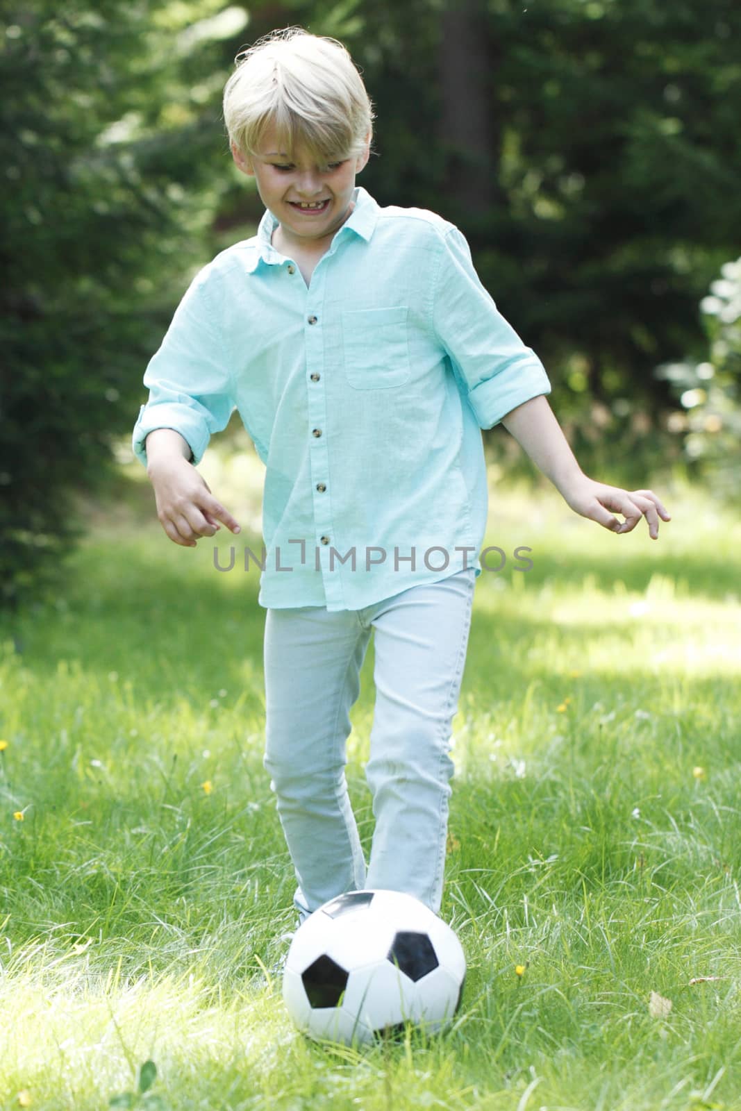 Happy smiling child boy playing football in summer park