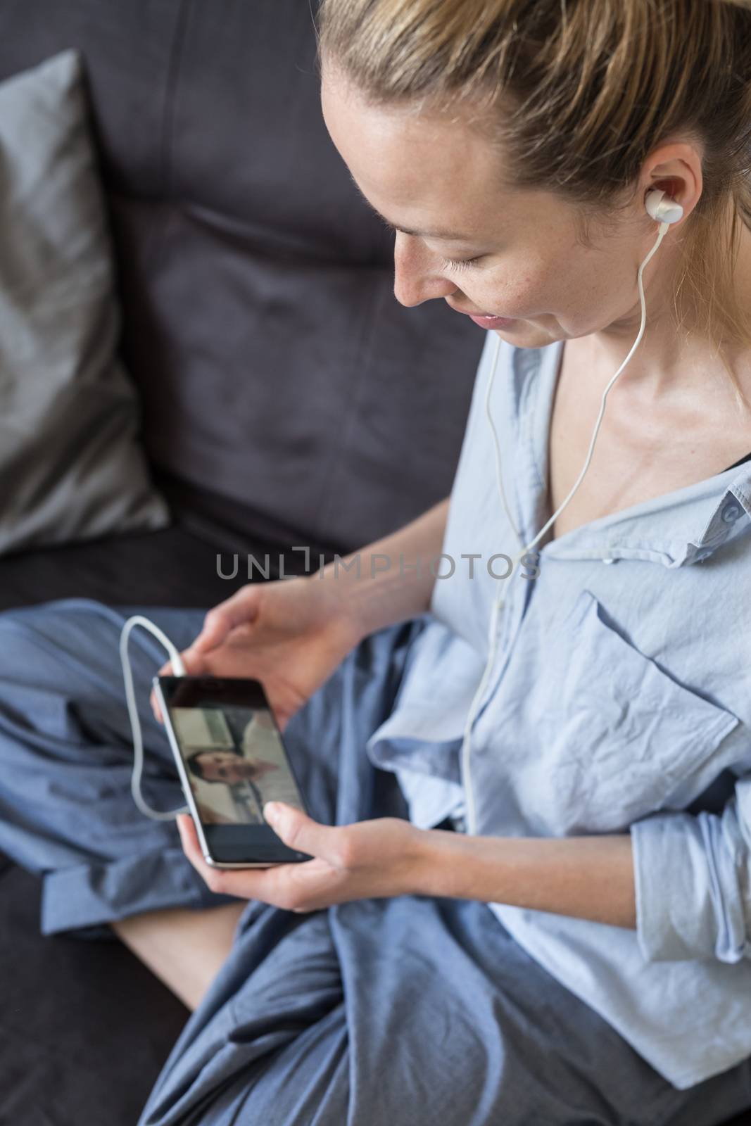 Stay at home, social distancing lifestyle. Woman at home relaxing on sofa couch using social media on phone for video chatting with her loved ones during corona virus pandemic.