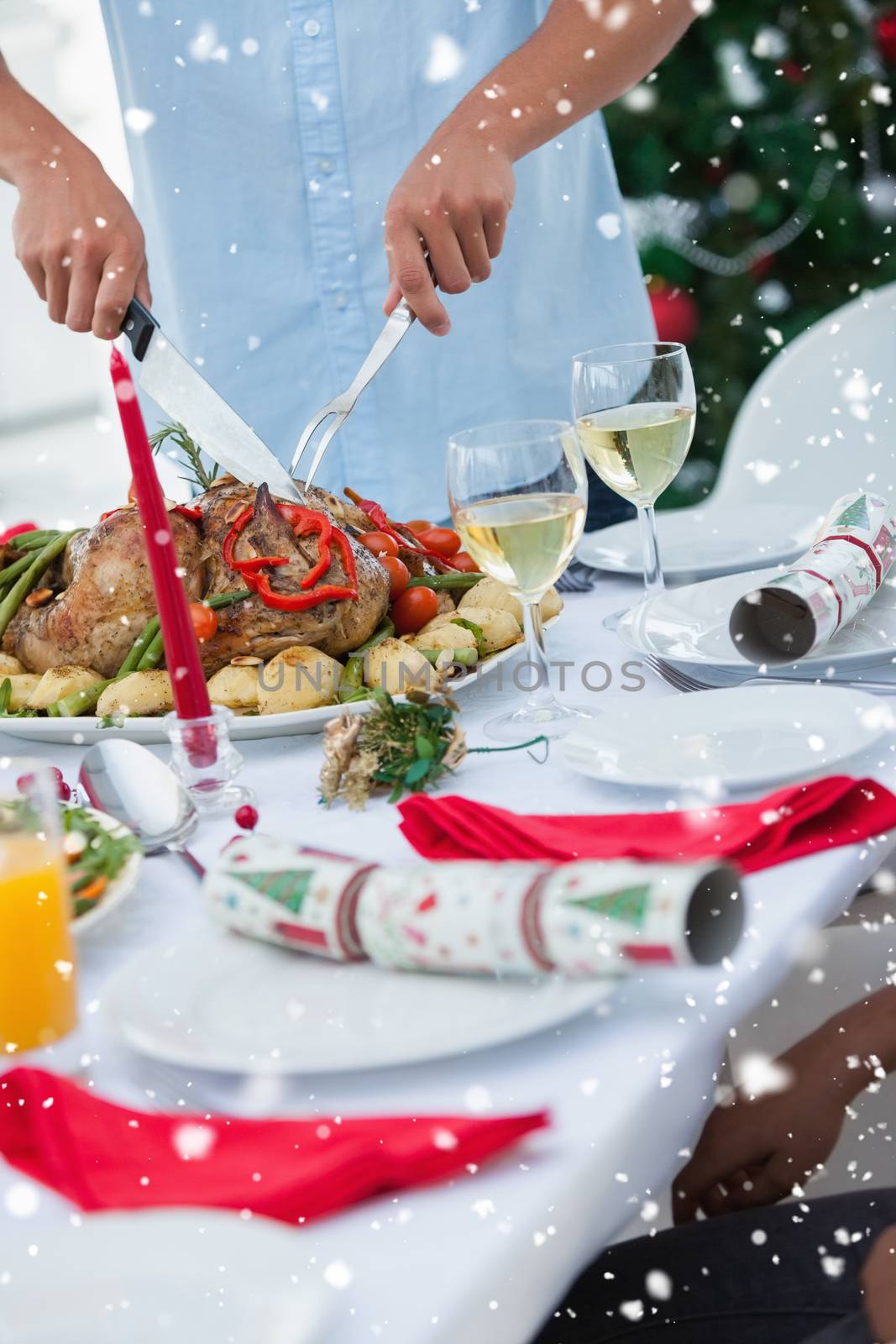 Man carving roast chicken at table against snow falling