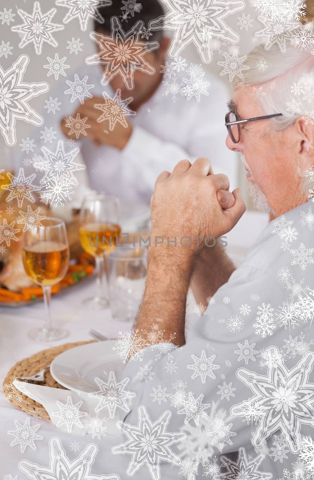 Family saying grace before eating against snowflakes on silver