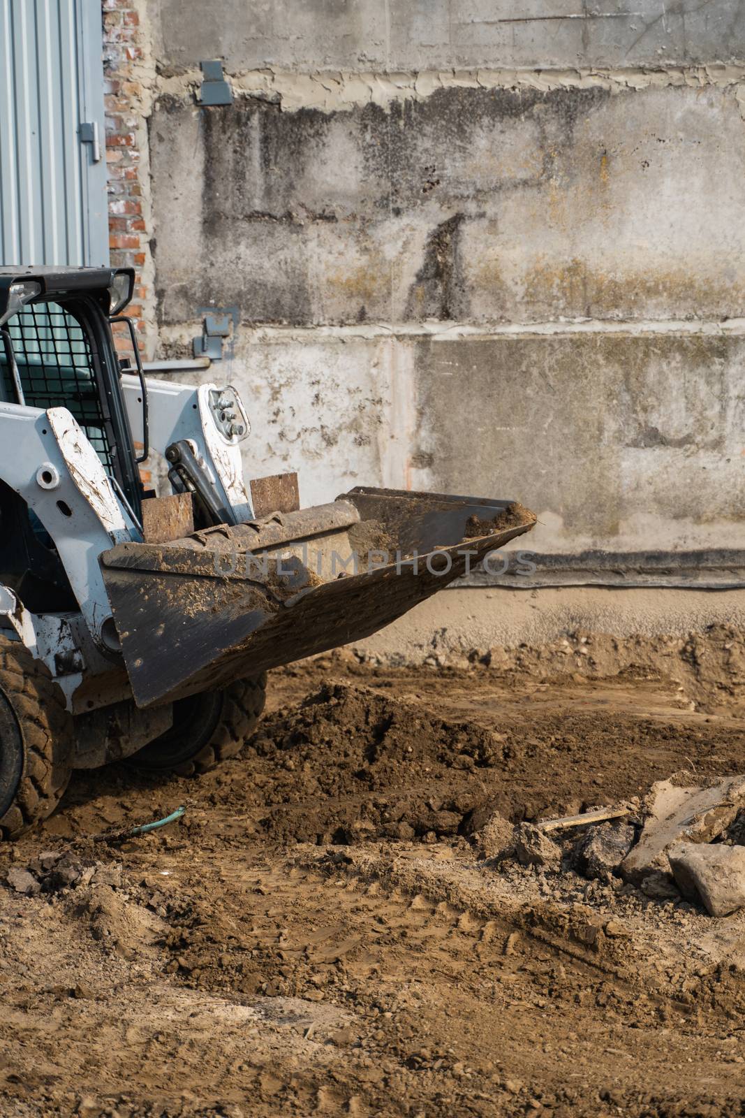 White skid steer loader at a construction site working with a soil. Industrial machinery. Industry