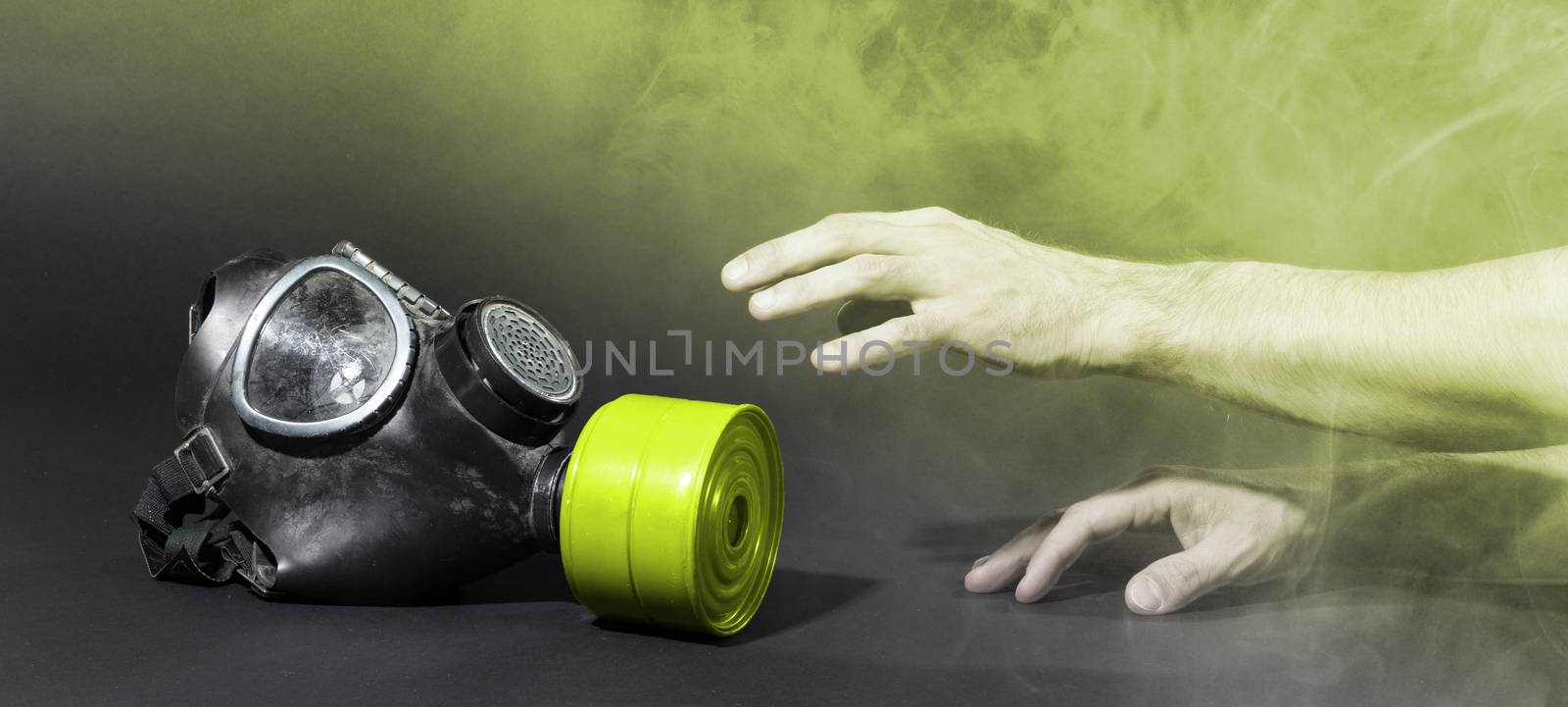 Man in room filled with smoke, trying to reach for vintage gasmask - Isolated on black - Yellow smoke