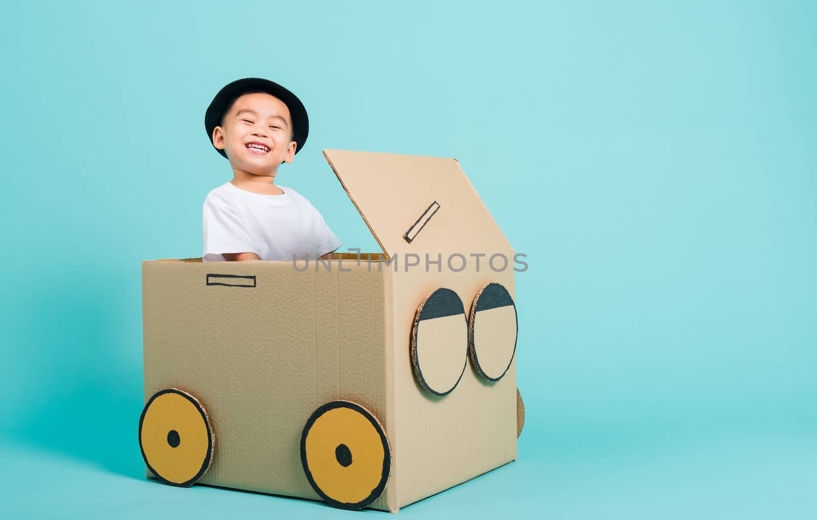 Happy Asian children boy smile in driving play car creative by a cardboard box imagination, summer holiday travel concept, studio shot on blue background with copy space for text