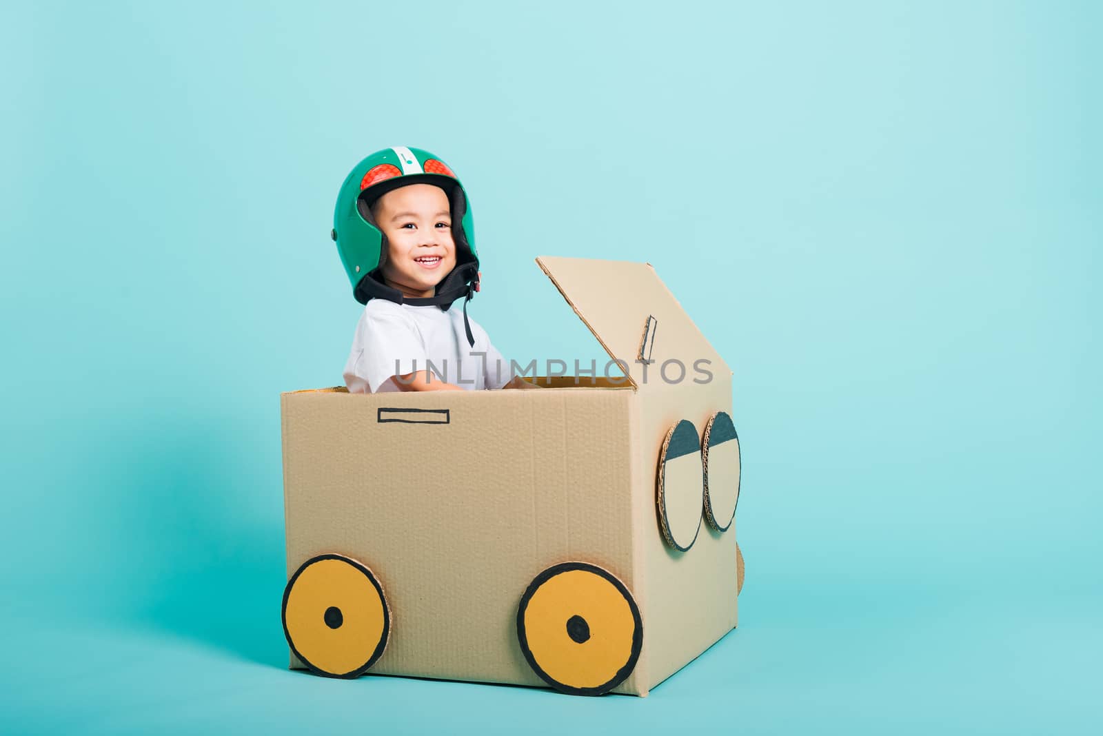 Happy Asian children boy with Helmet smile in driving play car creative by a cardboard box imagination, summer holiday travel concept, studio shot on blue background with copy space for text