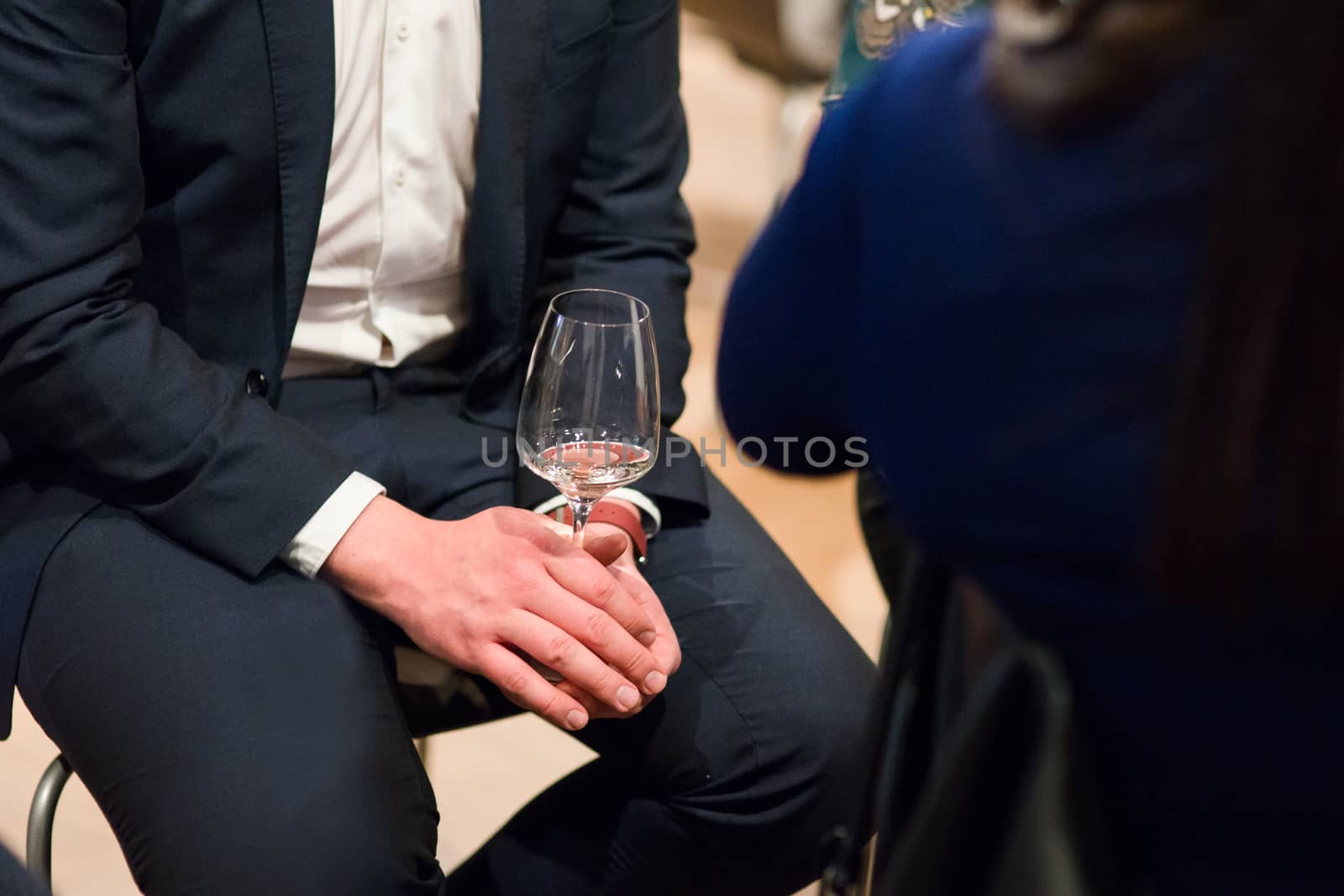 Man in suite sitting holding a glass of white wine, body parts photographed on a wine tasting event. by tamas_gabor