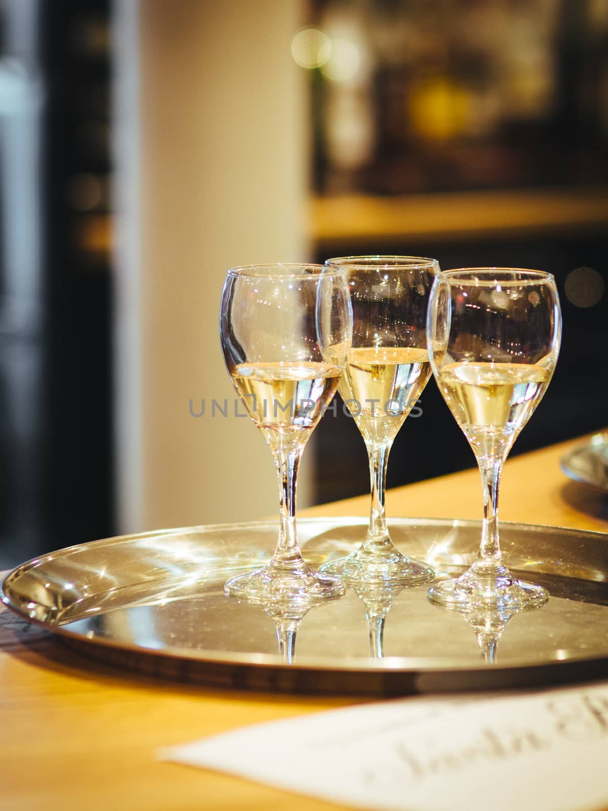 Interior shot of three glasses of white wine on a silver metallic tray placed on the table with blurred background in artificial lightning. by tamas_gabor