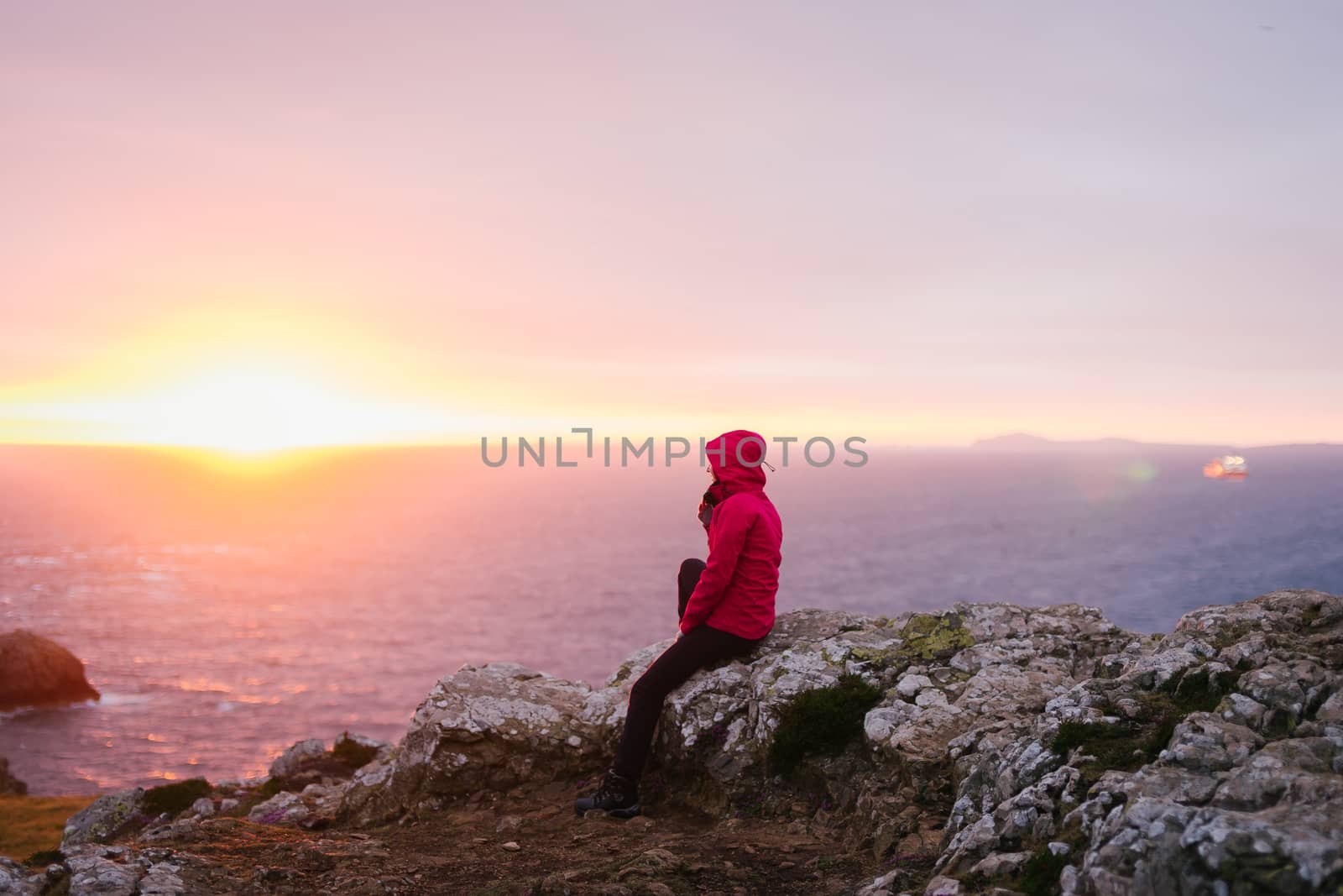 Woman sitting on the rocks watching the sunset in Martin's Haven with St. Brides Bay in the background - Pembrokeshire, West Wales.