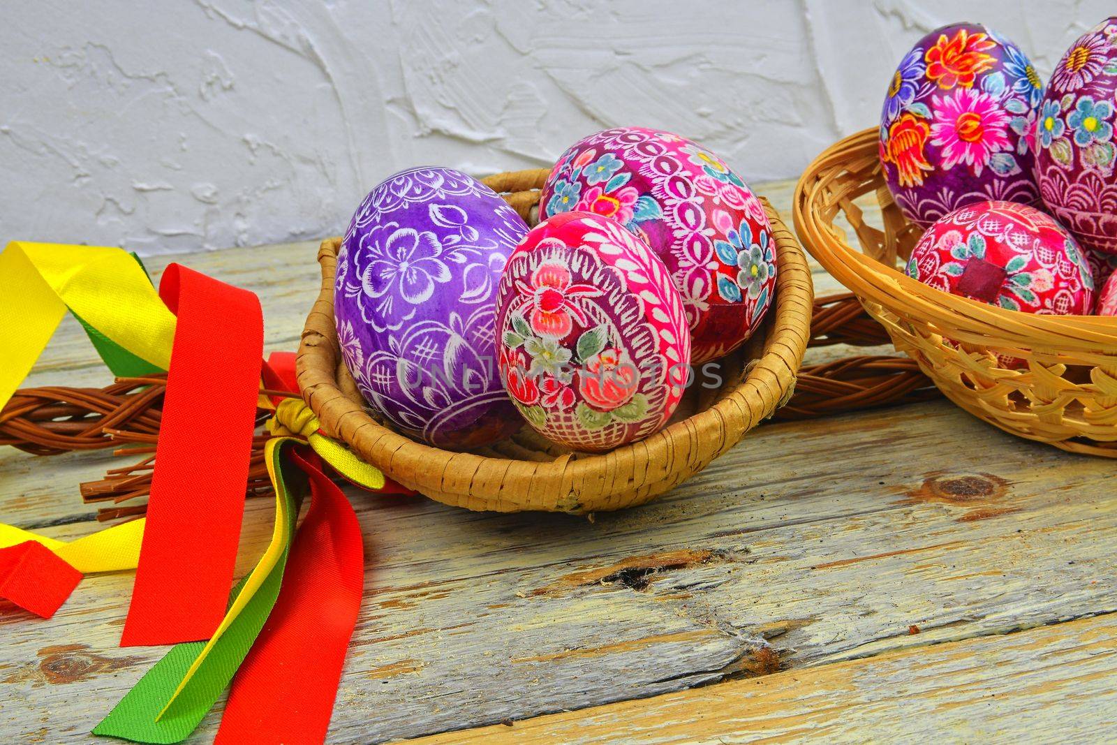 Still life with Easter eggs.  Decorated Easter eggs lay in a wicker basket on a white wooden background. Easter eggs, decorated with traditional folk designs - east Europe, Czech Republic