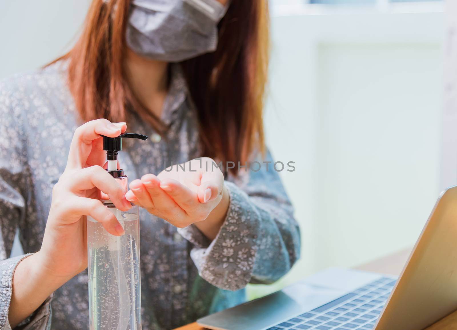 Asian Business young woman working from home office he quarantines disease coronavirus or COVID-19 wearing a protective mask and cleaning hands with sanitizer gel on front laptop computer