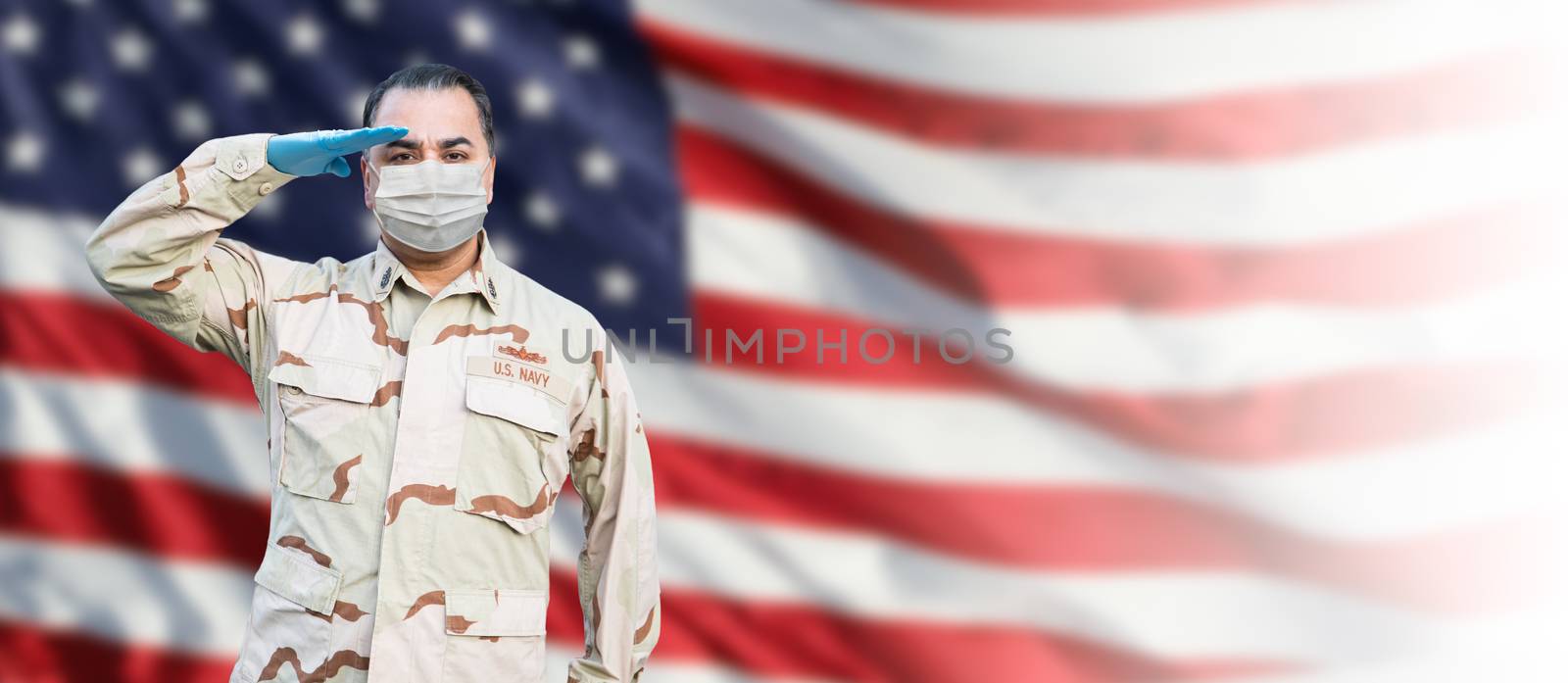 Male Navy Medical Personel Saluting Wearing Personnel Protective Equipment (PPE) With American Flag Background Banner.