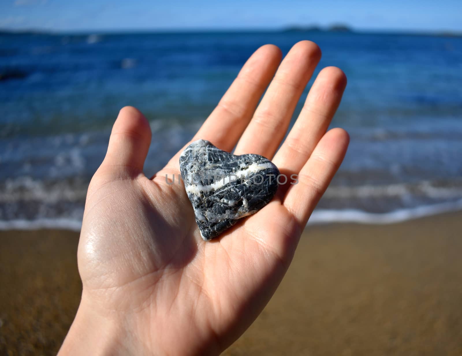 A female holding a black and white heart shaped rock at the beach