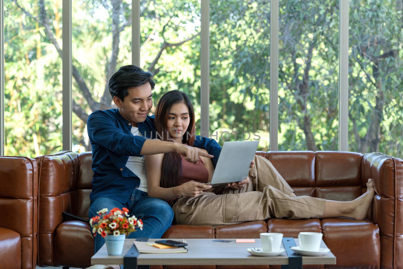 Young lovers spend time together on holidays in the living room. Both of them are interested in internet product information while the girl held laptop computer.