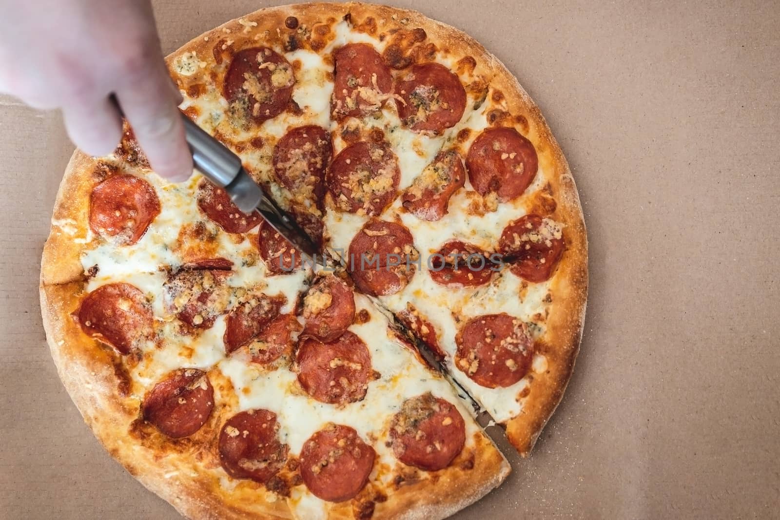 cropped male hand cuts pizza margarita with pepperoni with a special knife, closeup. Top view, copy space by Tanacha