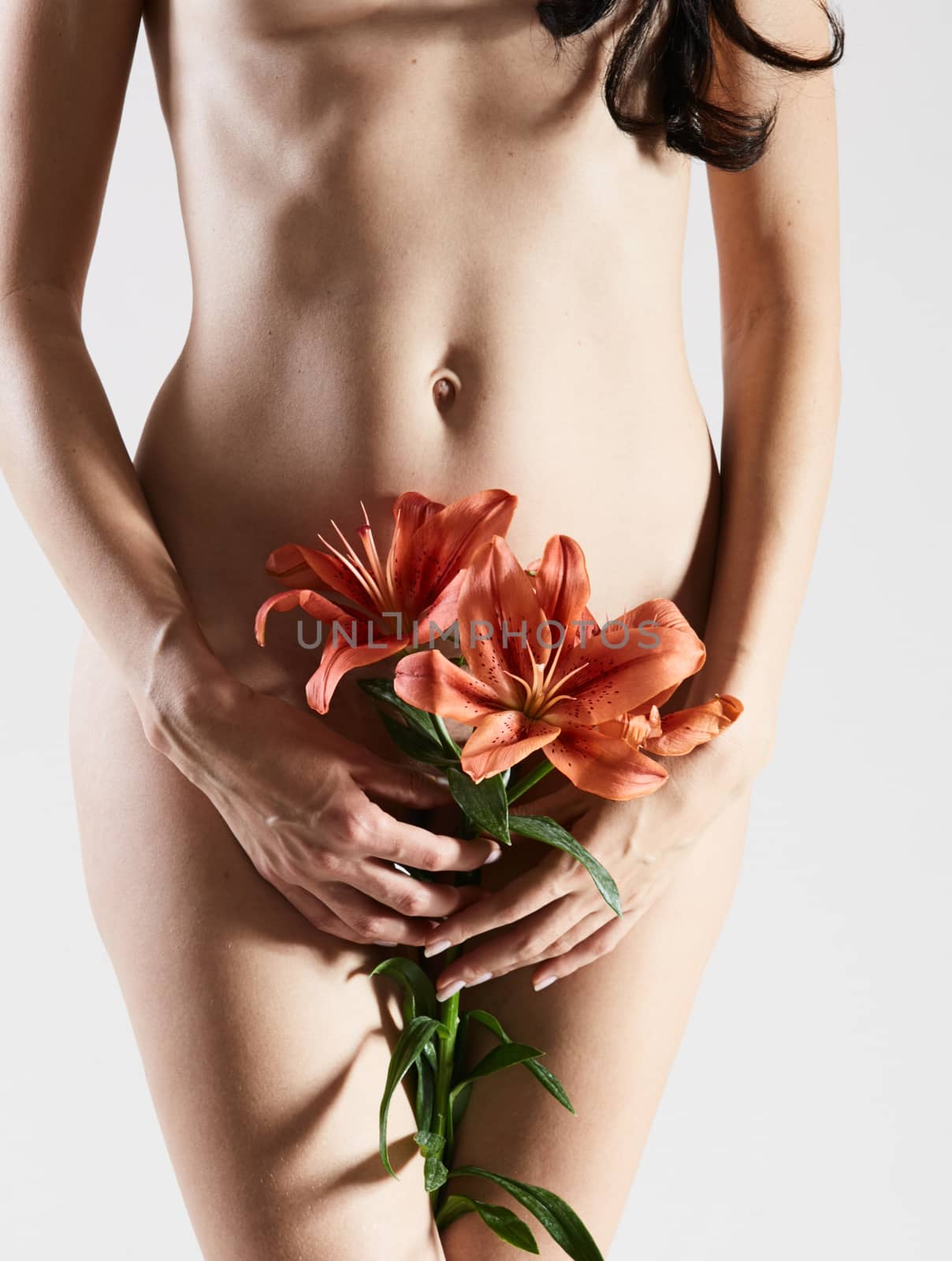 Intimate part of a woman's body with flower in hands. Close up of a woman body with flower on her pubes. No retouch