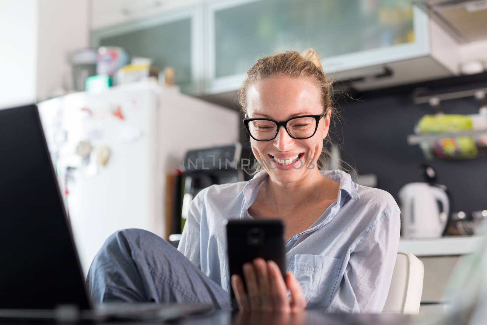 Stay at home and social distancing. Woman in her casual home clothing working remotly from kitchen dining table. Video chatting using social media with friend, family, business clients or partners.