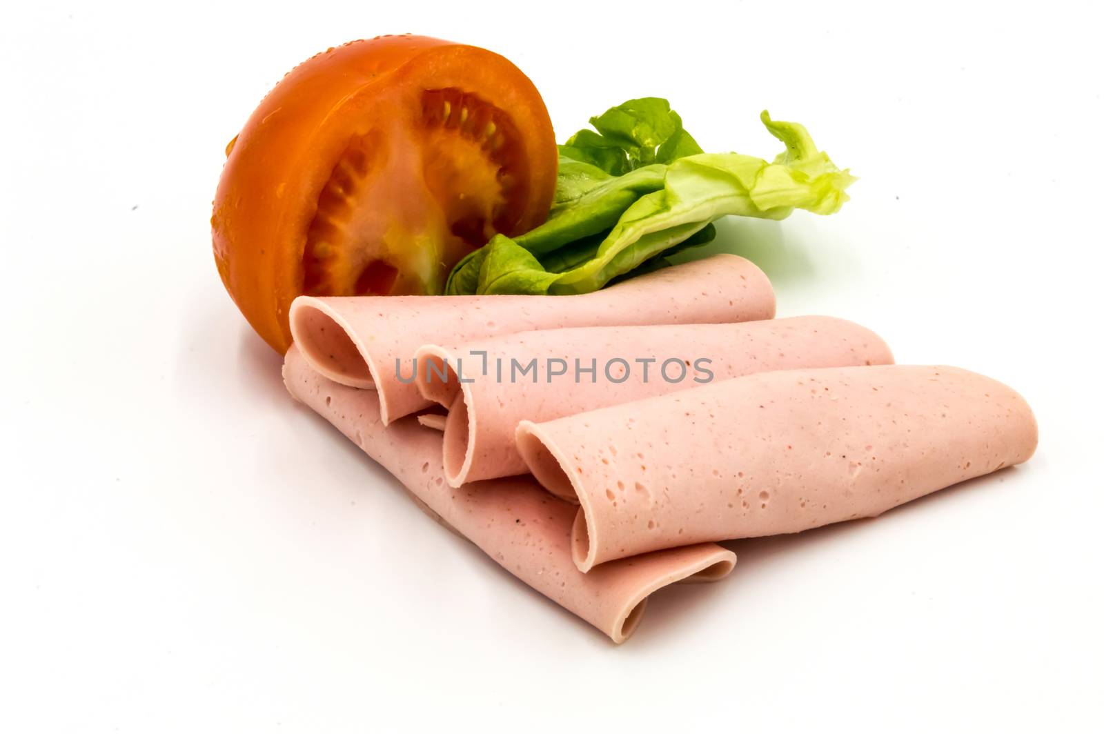 Slice of ham or Paris sausage on a white background with half a tomato and a salad leaf