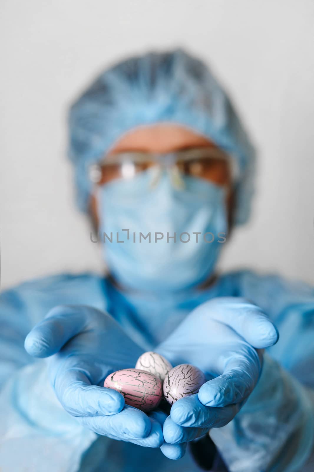 Hands in medical gloves holding modern painted easter eggs. Selective focus. Toned picture.