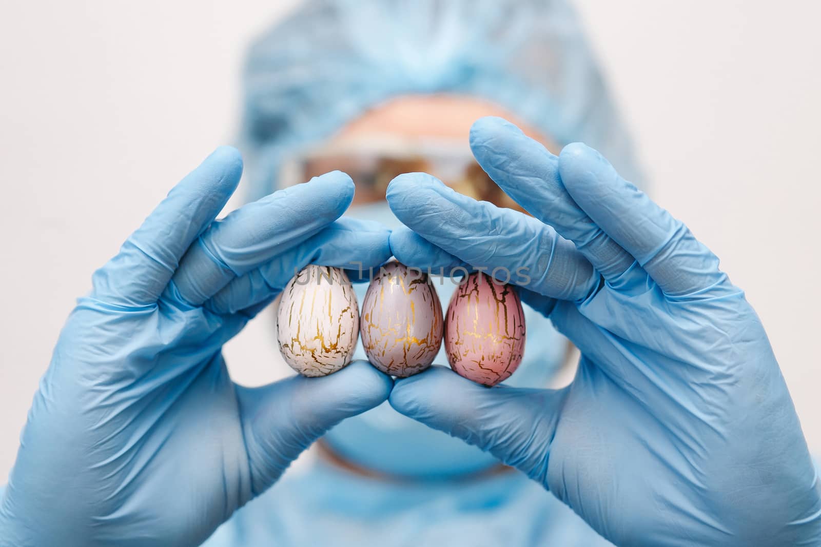 Hands in medical gloves holding modern painted easter eggs. Selective focus. Toned picture.