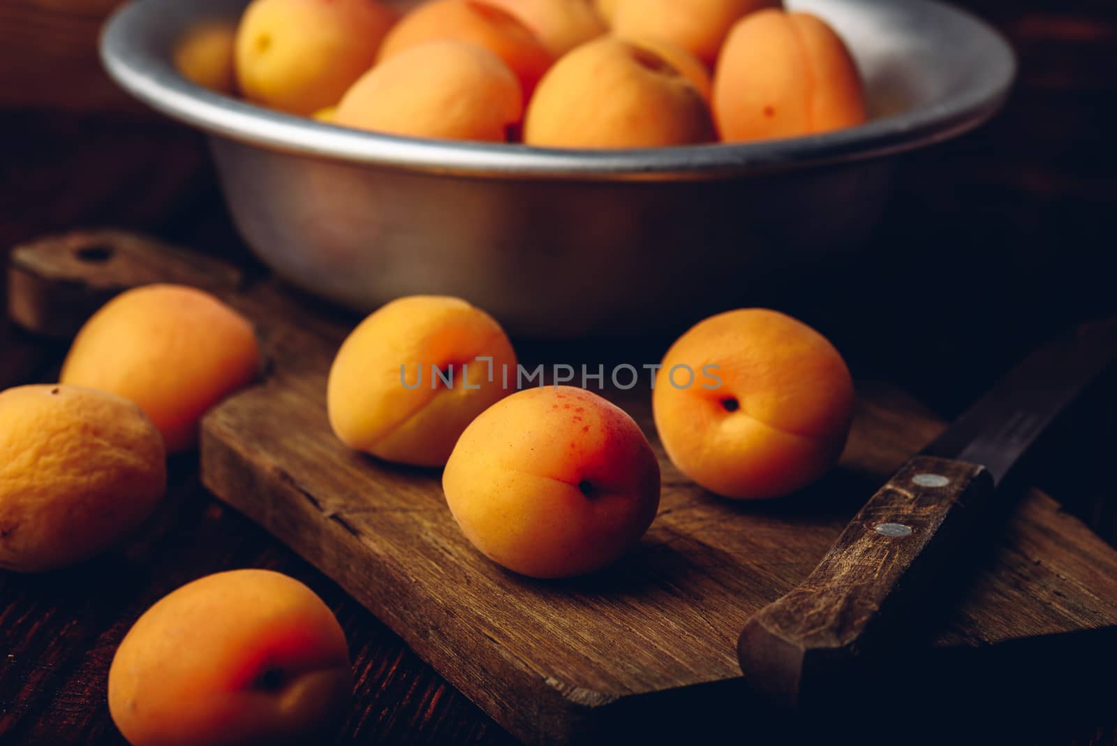 Mellow apricots with knife over old wooden cutting board and metal bowl with fruits