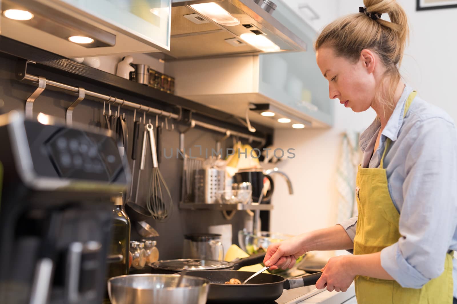 Stay at home housewife woman cooking in kitchen, salting dish in a saucepan, preparing food for family dinner. Blonde caucasian model in her 30is, real cooking not looking in camera.