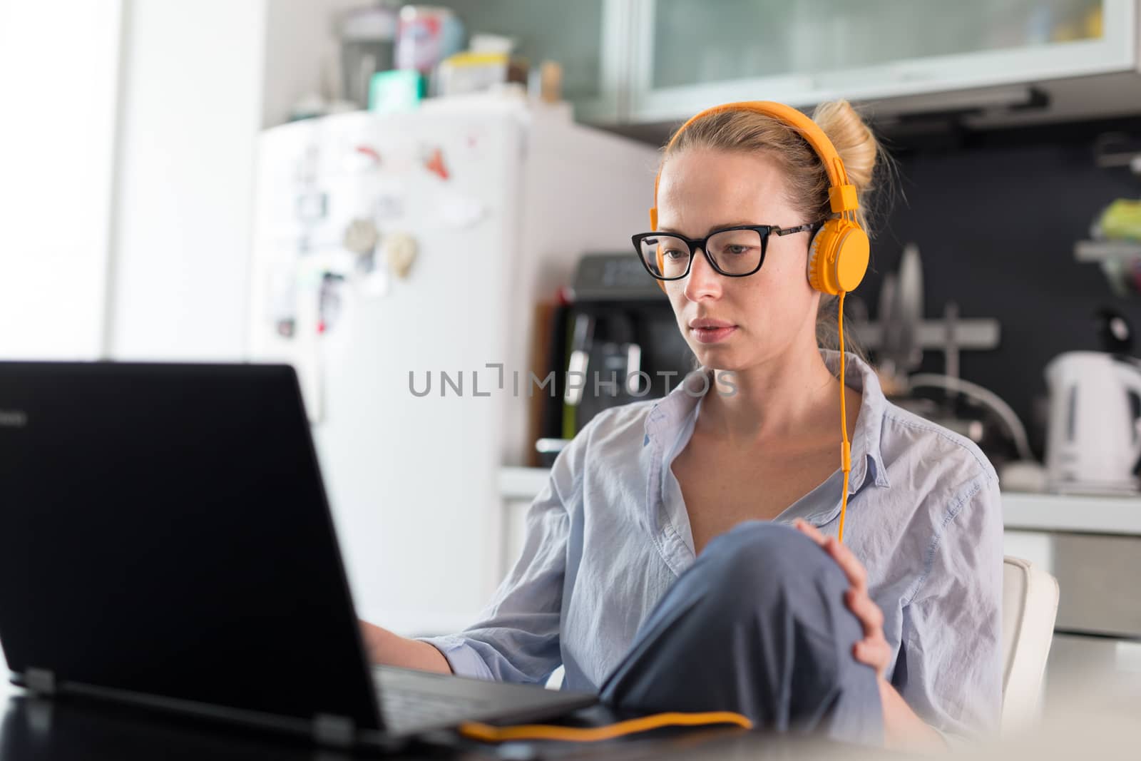 Female freelancer in her casual home clothing working remotly from her dining table in the morning. Home kitchen in the background. Stay healthy and stay at home during corona virus pandemic.