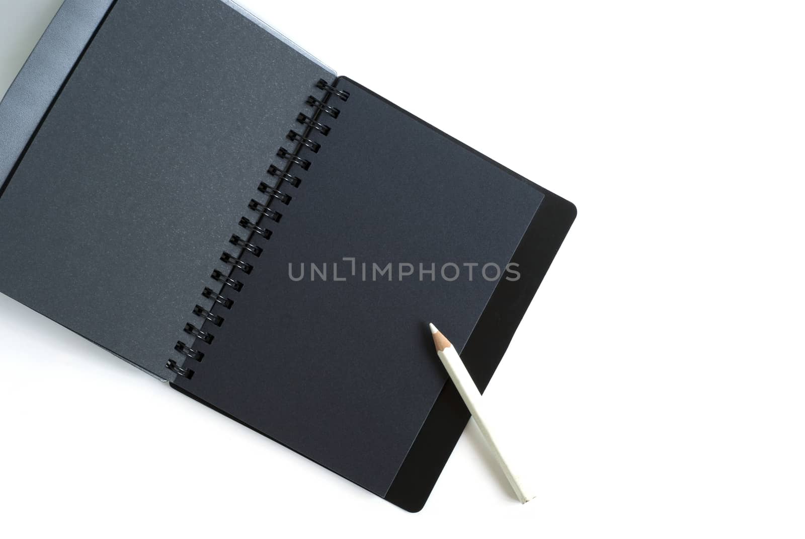 Black paper spiral notebook and white pencil by Satakorn