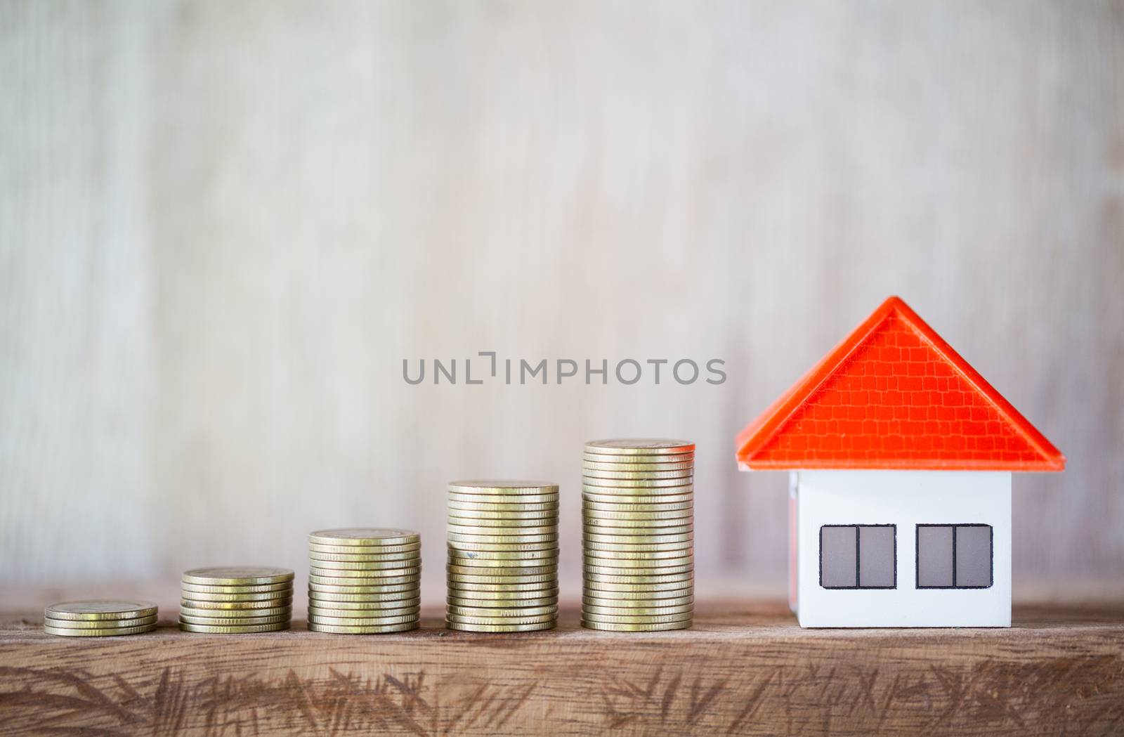 Stack of coins In order from low to high.And an orange roof model house on a wooden table. Money saving concept Business growth Saving money for investment. Save money for housing in the future.