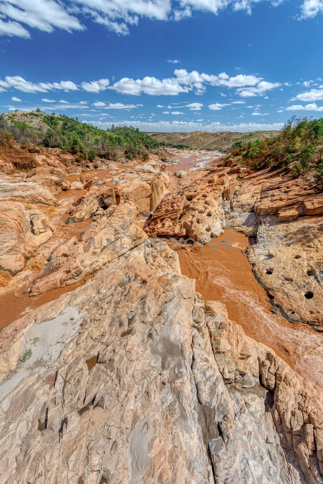 rocky river bed Betsiboka river after heavy rain, red yellow water stream, landscape with blue sky, northern Madagascar landscape, Africa wilderness