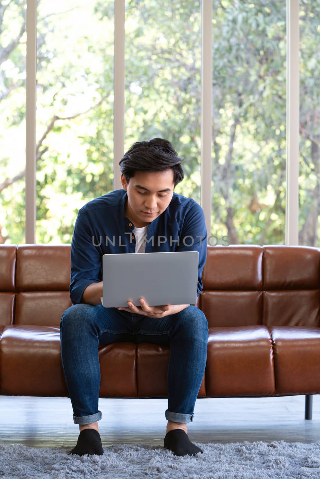 Asian man spend holidays in the living room. The young man wore comfortable clothes use laptop computer to search for jobs.