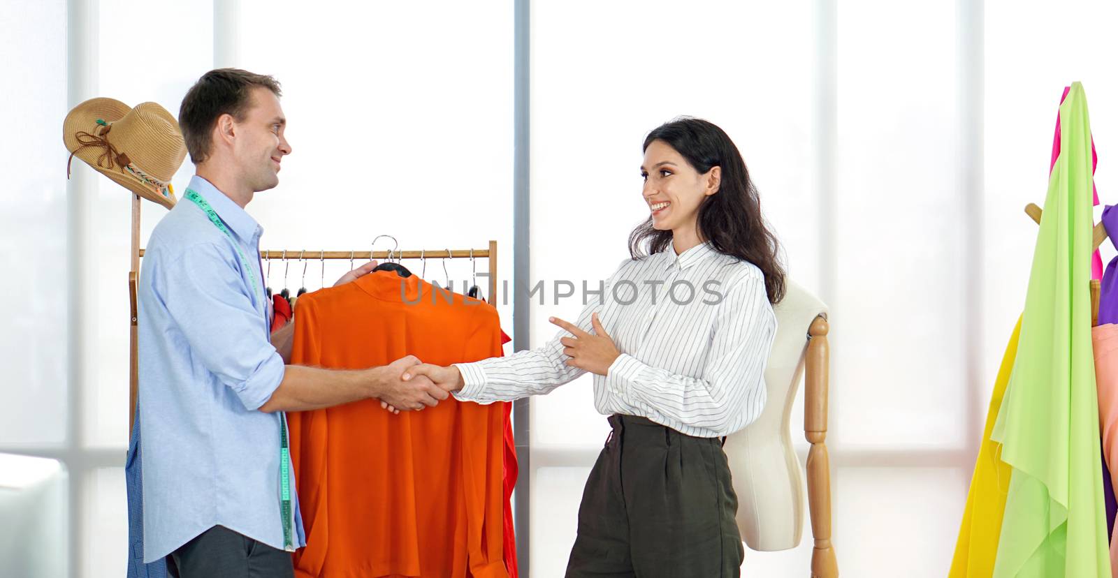 The young client shook hands with the designer in the tailor's room. Fashion designer room, man and woman working in home base cloth design business.