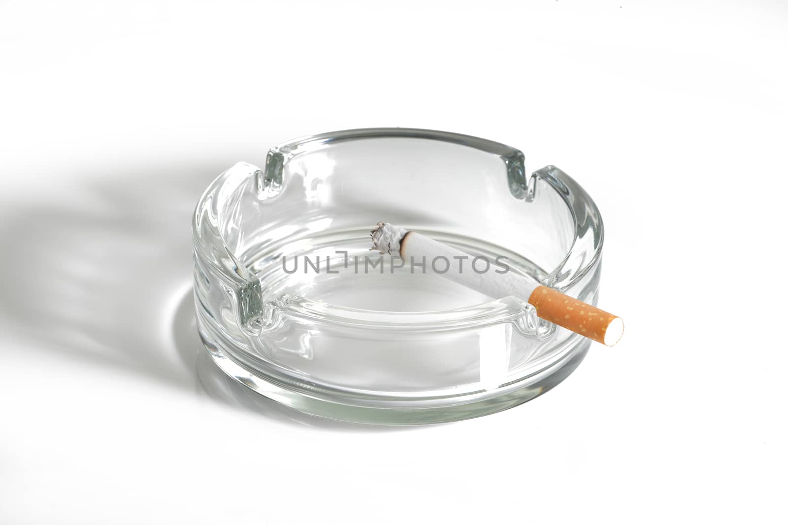 A cigarette lit in glass ashtray on white