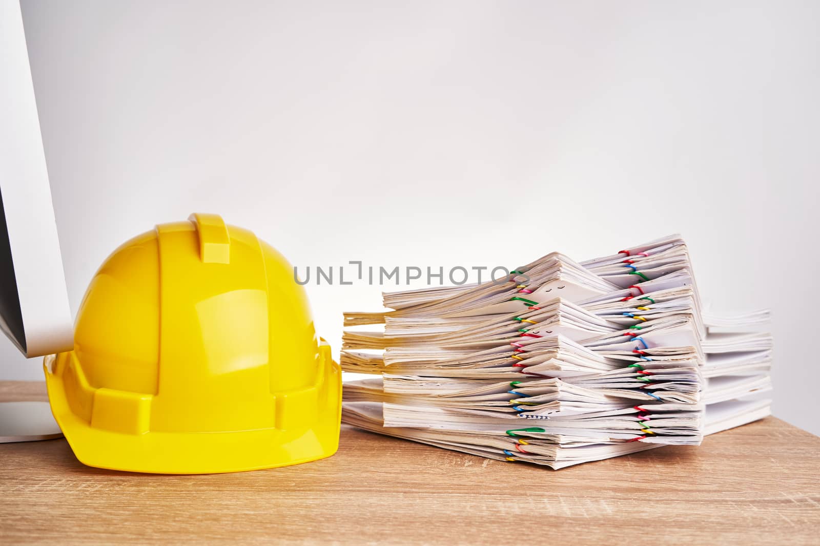 Stack overload document of report and receipt with colorful paperclip with yellow engineer hat on wooden computer table with white background and copy space. Industrial successful concept photography.