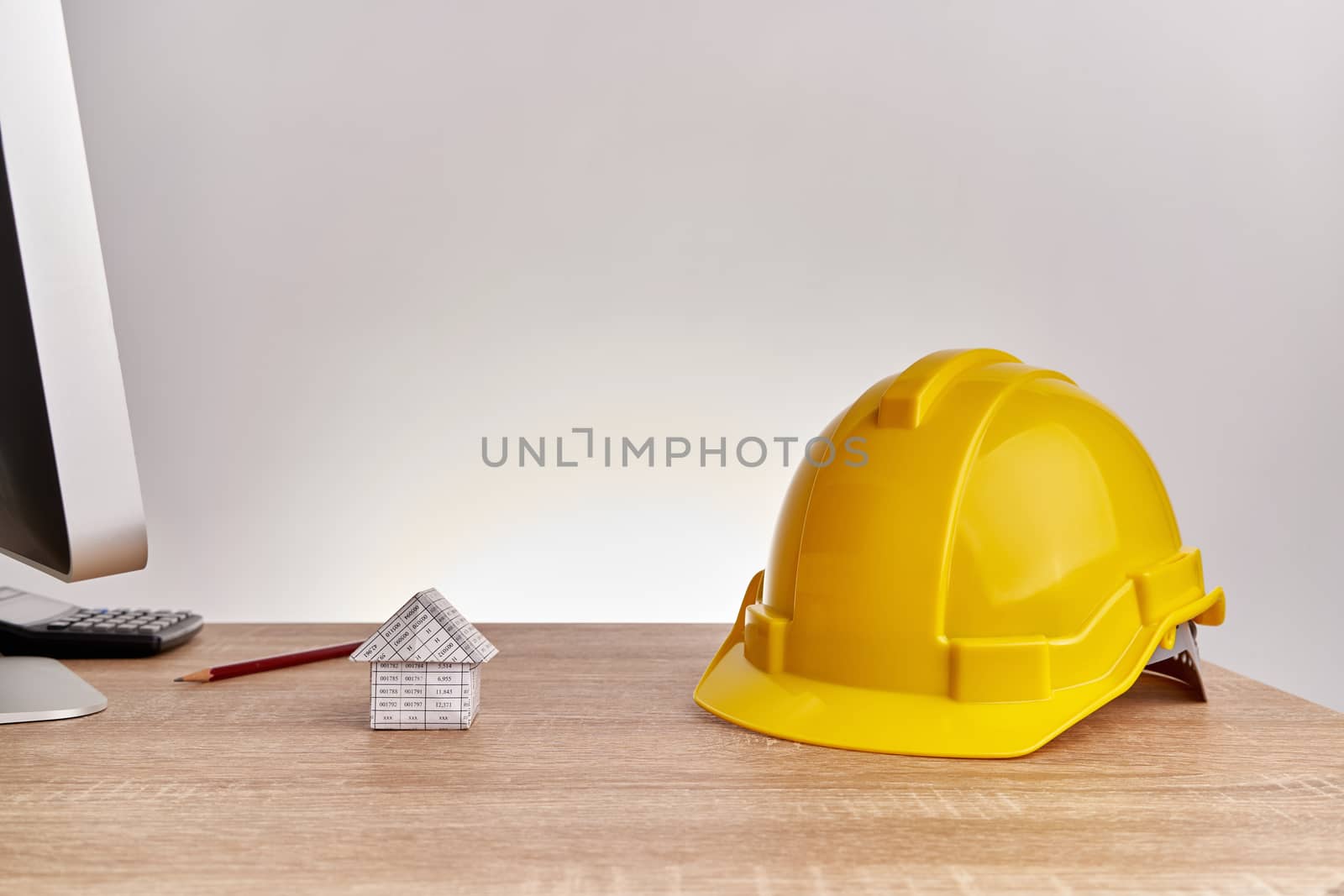 Yellow engineer hat and house  have blur brown pencil and calculator on wooden computer table with white background and copy space. Industrial successful concept photography.