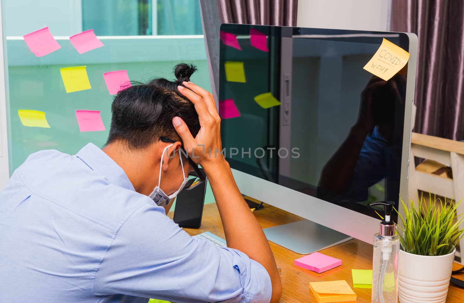 Tired business young man wearing a protective mask with disinfectant gel beside, work from home office with computer he strain hands holding temples, quarantines disease coronavirus or COVID-19