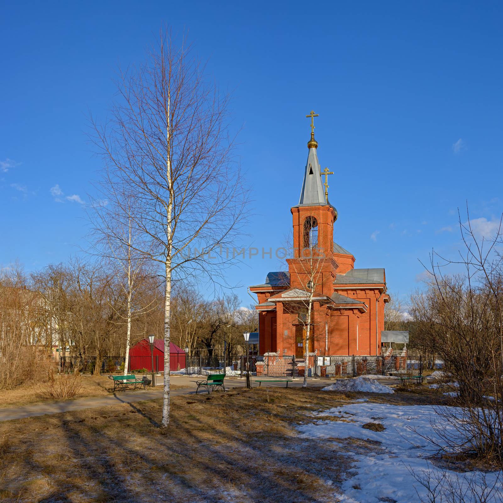The Orthodox church of red brick surrounded by trees under a blue sky lit by the evening light of the sun in spring.