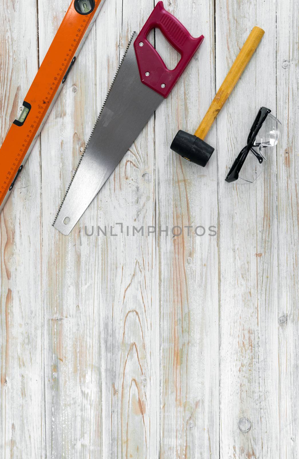 The equipment for woodworking is organized neatly on the wood floor. Ordered as follows, Orange Magnetic aluminum level, Red Hand Saw, Yellow mallet, Black Dustproof glasses. 