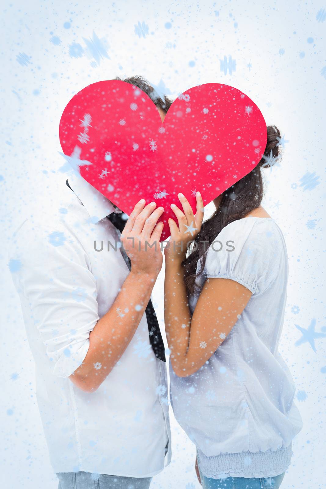 Couple covering their kiss with a heart against snow falling